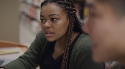 A young Black woman in a green sweater and long braids
