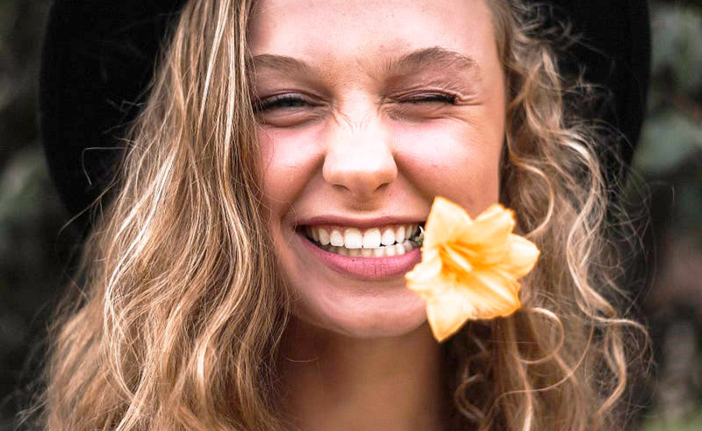 young woman with flower in her teeth, smiling and winking