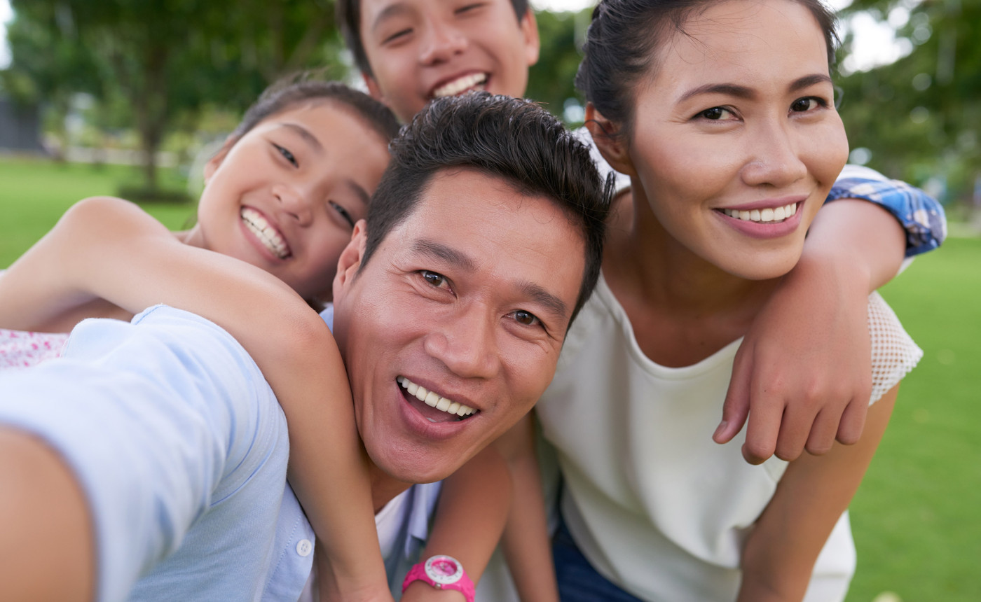 smiling southeast asian couple with two young children outside in a park