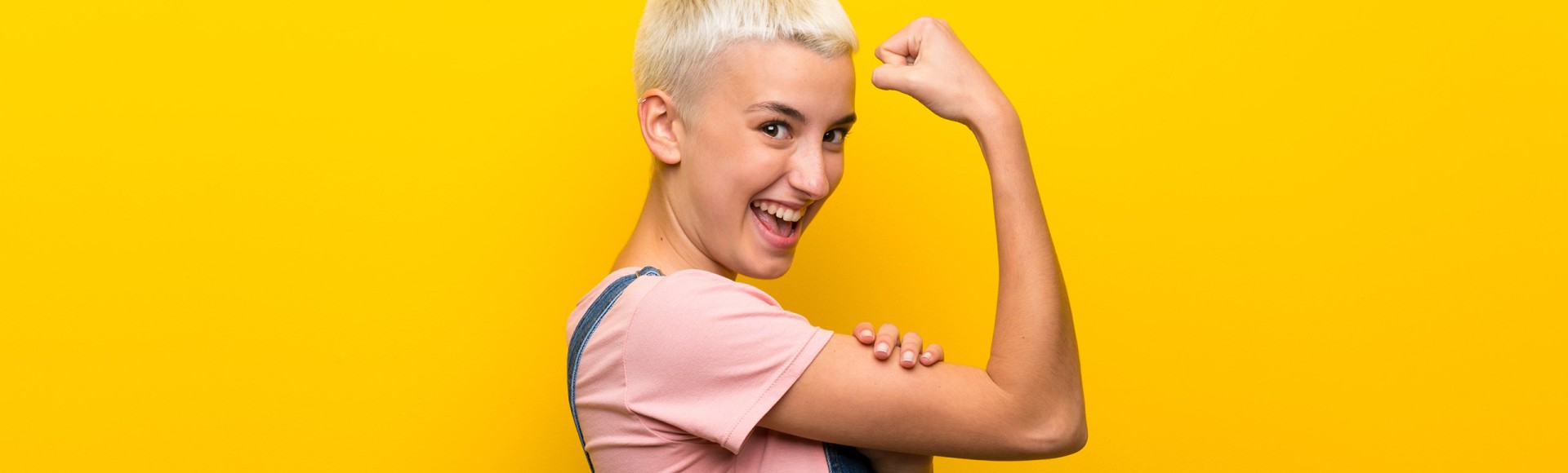 young woman in overalls flexing her biceps