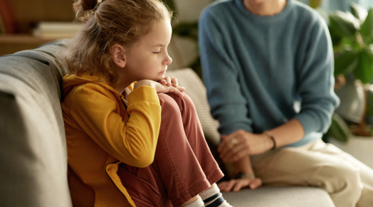 Little boy sitting on sofa without mood and having no desire to talk to his mom