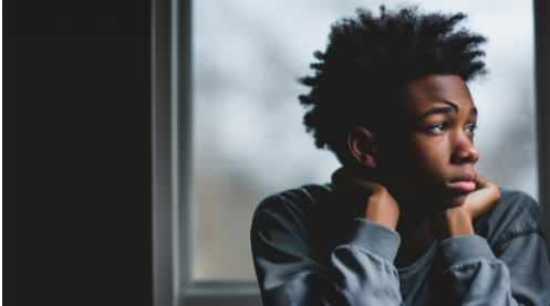 Despondent black young man looking out window.